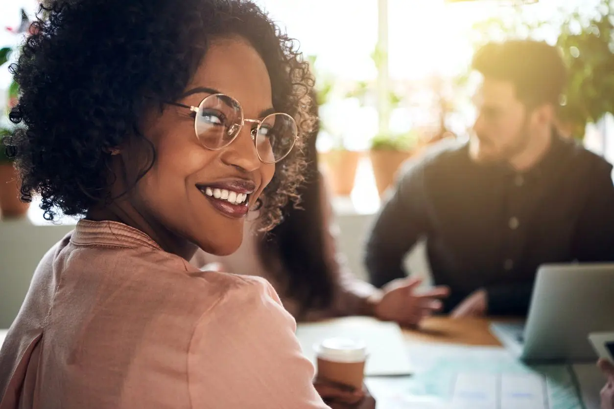 Smiling woman with glasses in a casual meeting setting.